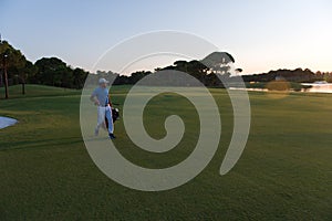 Golfer walking and carrying golf bag at beautiful sunset