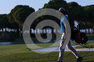 Golfer walking and carrying golf bag at beautiful sunset