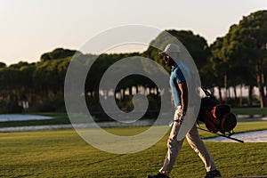 Golfer walking and carrying golf bag at beautiful sunset