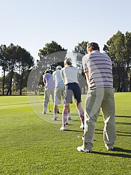 Golfers Standing In Row Teeing Off