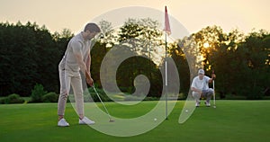 Golfers team hitting ball on sunset field course. Two players missing golf shot.