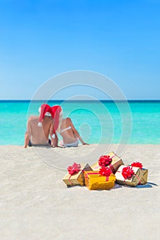 Golgen gifts and couple in Christmas Santa hats at beach