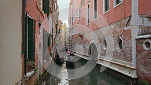 Gondola go down canal at day, Venice, Italy. Gondolier navigate boat. Tourists enjoy ride and take photos. Medieval