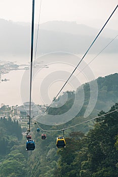 Gondola lifts moving over mountain with green trees in the area of Sun Moon Lake Ropeway in Yuchi Township, Nantou County, Taiwan