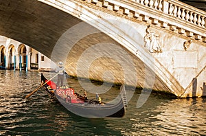 Gondola passing under the Rialto Bridge at sunset in Venice, Italy