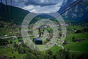 Gondola riding above the green field, buildings and mountains of Switzerland