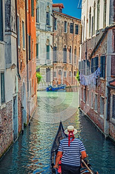 Gondola sailing narrow canal in Venice between old buildings with brick walls. Gondolier
