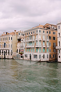 A gondola with tourists is sailing along the Grand Canal amid the facades of Venetian houses standing on the water in