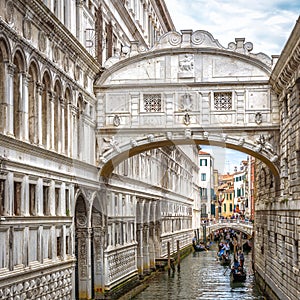 Gondolas with tourists sails on old canal under medieval Bridge of Sighs by Doge`s Palace, Venice