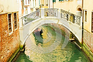 Gondolier in boat passing below bridge in venice canal