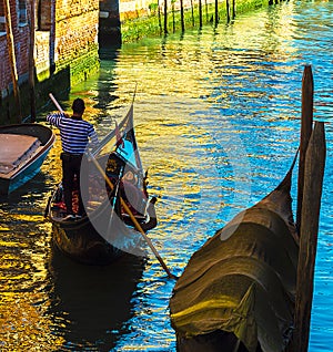 Gondolier rowing on his gondola in a Venetian canal on a summer day