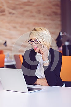 Good business talk. Cheerful young beautiful woman in glasses talking on mobile phone and using laptop