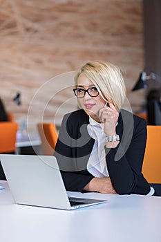 Good business talk. Cheerful young beautiful woman in glasses talking on mobile phone and using laptop