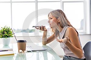 Good business talk. Cheerful young beautiful woman in glasses talking on mobile phone and using laptop with smile while sitting at