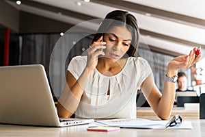 Good business talk. Cheerful young beautiful woman talking on mobile phone and using laptop with smile while sitting at