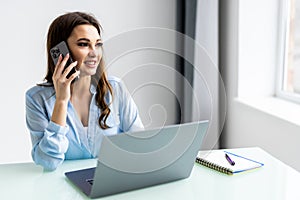 Good business talk. Cheerful young woman in glasses talking on mobile phone and using laptop with smile while sitting at her