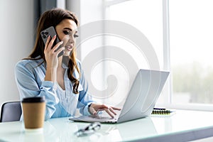 Good business talk. Cheerful young woman in glasses talking on mobile phone and using laptop with smile while sitting at her