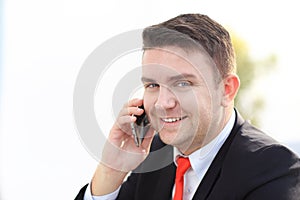 Good business talk. Handsome young man in formalwear talking on the phone and smiling while sitting photo