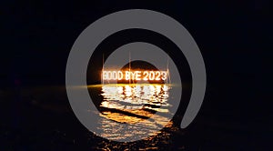 Good bye 2023 illuminated sign installation in water on the beach on black background. Old year is burning. Happy winter holidays