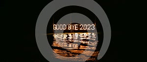 Good bye 2023 illuminated sign installation in water on the beach on black background. Old year is burning. Happy winter holidays