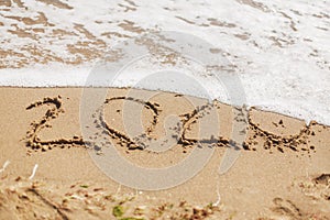 Good bye 2020 ! Wave with foam covering 2020 sign on sandy beach, leaving awful year 2020 photo