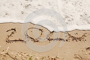 Good bye 2020 ! Wave with foam covering 2020 sign on sandy beach, leaving awful year 2020