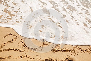 Good bye 2020 ! Wave with foam covering 2020 sign on sandy beach, leaving awful year 2020