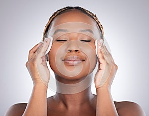 A good cleanser in underrated. Studio shot of an attractive young woman wiping her face with cotton against a grey