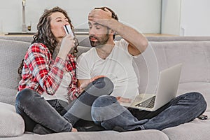 A good couple while shopping online using a laptop and smiling while sitting at a couch at home.