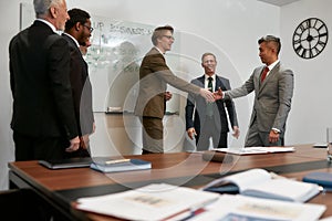 Good deal. Caucasian and Asian businessmen in classic wear shaking hands after signing the agreement while standing with