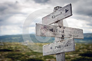 Good, evil and politics text on wooden sign post outdoors in landscape scenery.