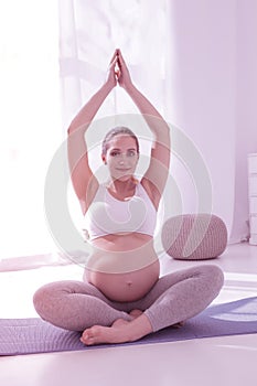 Young beaming long-haired pregnant woman in a white t-shirt looking contented