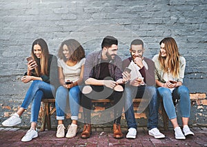 Good friends pass on good memes. a group of young friends using their mobile phones outdoors.