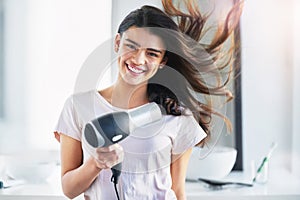 Good hair day, here I come. Portrait of a beautiful young woman blowdrying her hair in the bathroom at home.