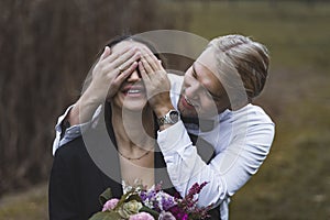 Good-humored young attractive Scandinavian groom in elegant white shirt covering the eyes of his newlywed Turkish wife