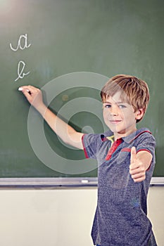 Good job. a little boy showing thumbs up while writing on the blackboard during a lesson.