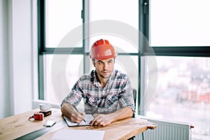 Good loking young man wearing red hardhat is preparing business plan