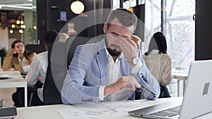 Good-looking 30s businessman putting off of glasses and rubing his eyes with fatigue during the work with computer in