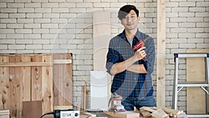 Good looking Asian carpenter standing while working for DIY jobs in carpenter room with several kinds of woods and types of