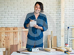 Good looking Asian carpenter wearing coverall dress working for DIY jobs in carpenter room with several kinds of woods and types
