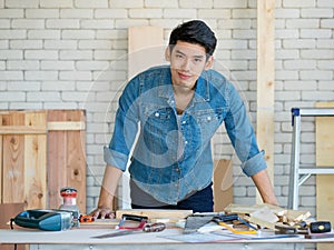 Good looking Asian carpenter working for DIY jobs in carpenter room with several kinds of woods and types of equipment
