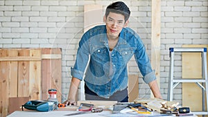 Good looking Asian carpenter working for DIY jobs in carpenter room with several kinds of woods and types of equipment