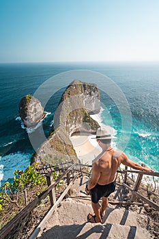 Good looking Asian  man traveller wearing hat and walking down to Kelingking beach in Nusa Penida island near Bali island in