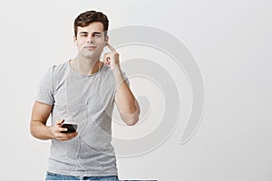 Good-looking attractive youngman in gray t-shirt having pleased look,holding mobile phone in his hand, wearing white