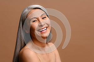 Good-looking beautiful middle-aged Asian woman posing in studio on brown background