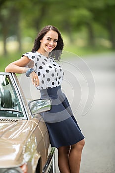 Good-looking brunette leaning her back and arm against a vintage cabriolet seductively looking into the camera