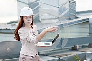 Good looking businesswoman in beige suit, brown trousers and helmet sit on the roof and hold laptop