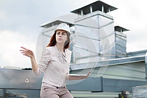 Good looking businesswoman in beige suit, brown trousers and helmet sit on the roof and hold laptop