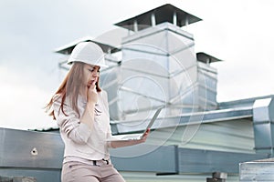 Good looking businesswoman in beige suit, brown trousers and helmet sit on the roof and hold laptop