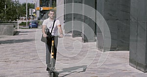Good-looking Caucasian businessman riding electric scooter near modern building. Successful adult male entreprenuer